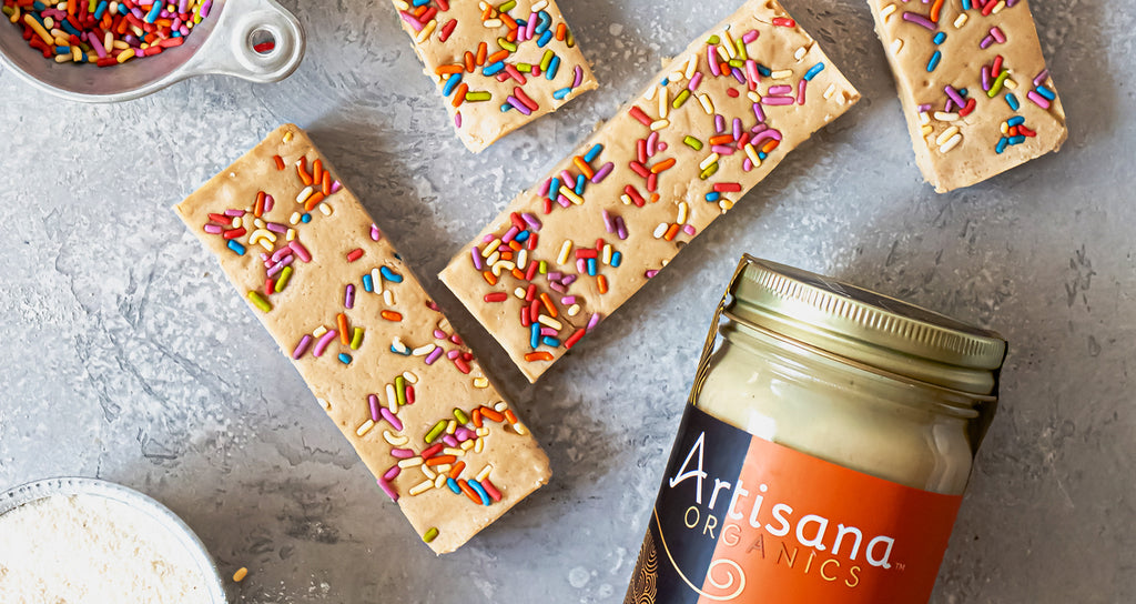 Birthday Cake flavor protein bars, with jar of Artisana cashew butter and cup of rainbow sprinkles