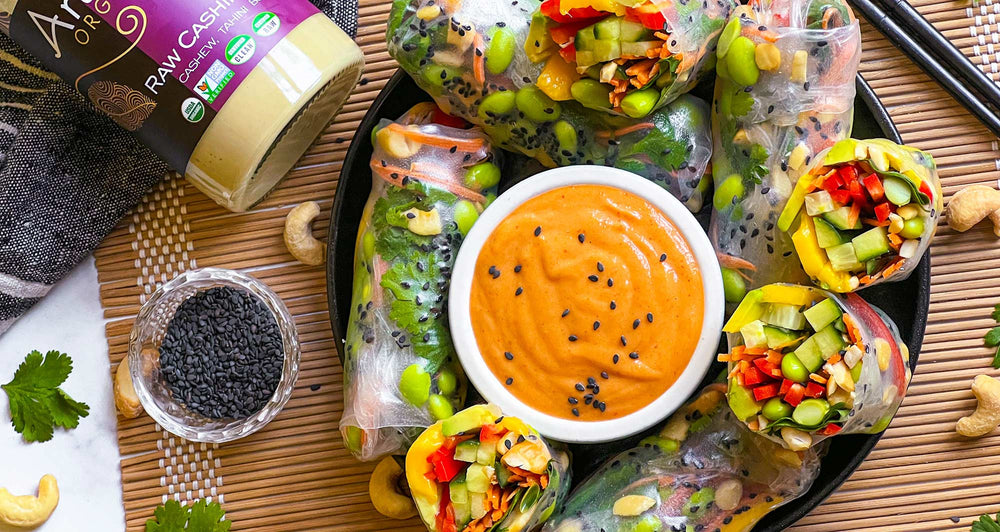 Whole and halved vegan Summer Rolls surrounding a small bowl of Spicy Cashini Sauce.