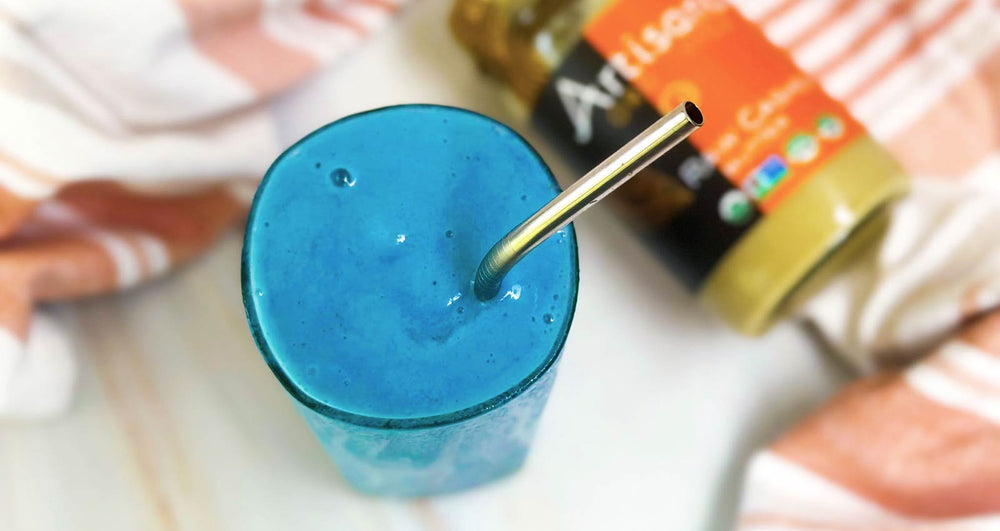A blue smoothie in a glass with a reusable straw.