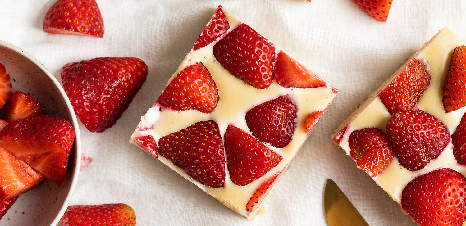 Strawberry cheesecake bars surrounded by sliced strawberries on a white background.