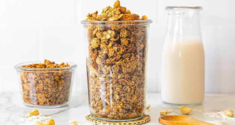 Granola in glass containers with a carafe of milk in the background.
