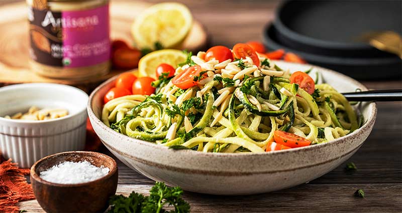 A delicious looking bowl of zoodle salad with nuts and tomatoes on top. 