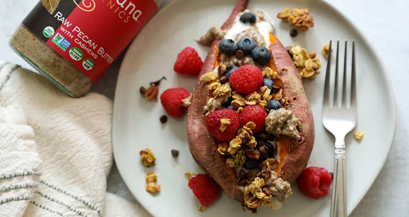A sweet potato on a plate. split in half and packed with yogurt, granola, and berries.